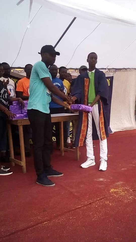 A volunteer shakes hands with a student in a graduation gown while presenting a wrapped gift.