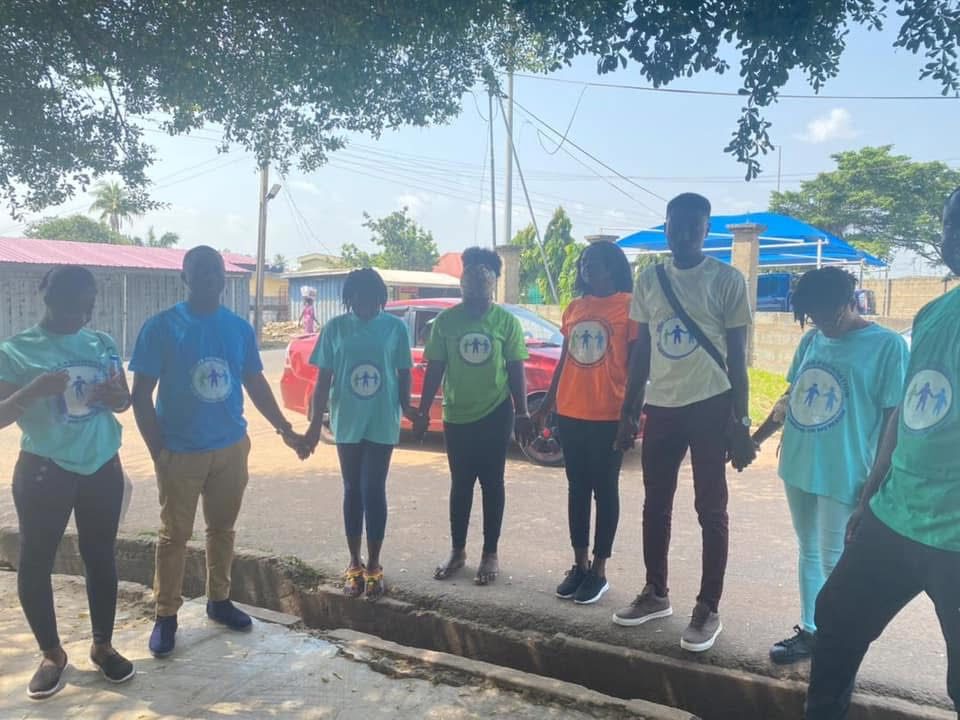 Volunteers in foundation T-shirts standing in a line holding hands by the roadside.