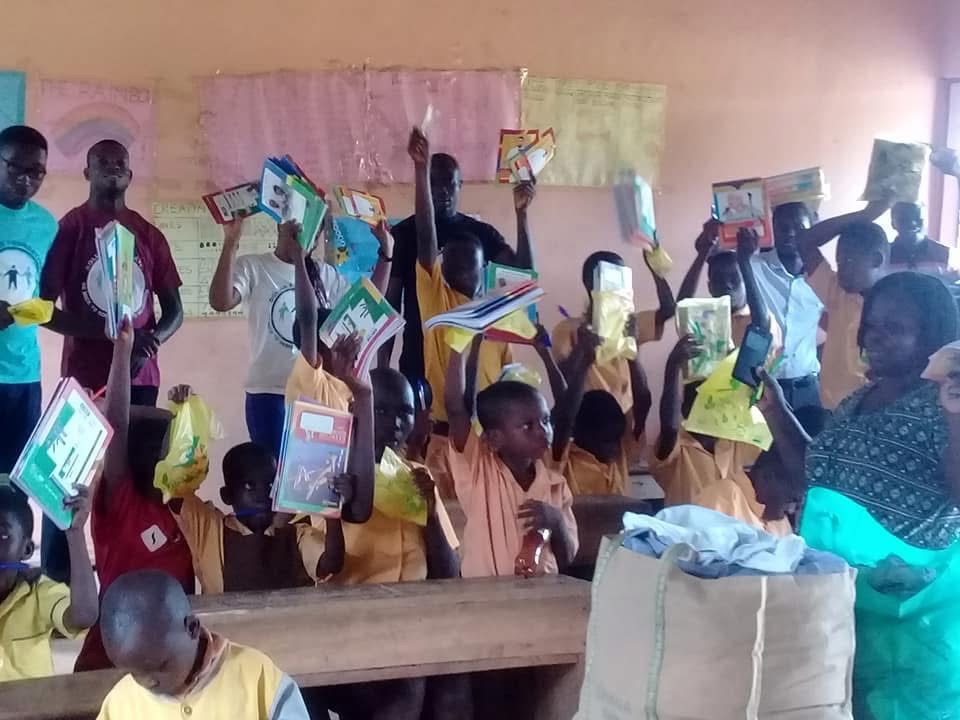 Pupils at their desks raise their new exercise books in the air as volunteers look on.