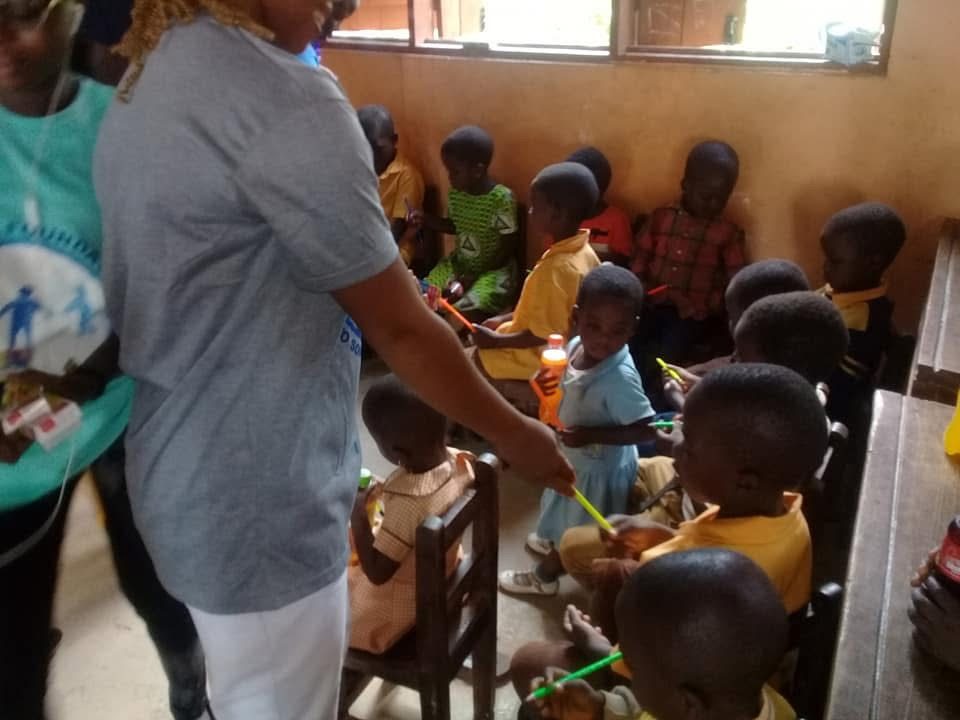A volunteer hands out pens to young pupils sitting in a classroom.