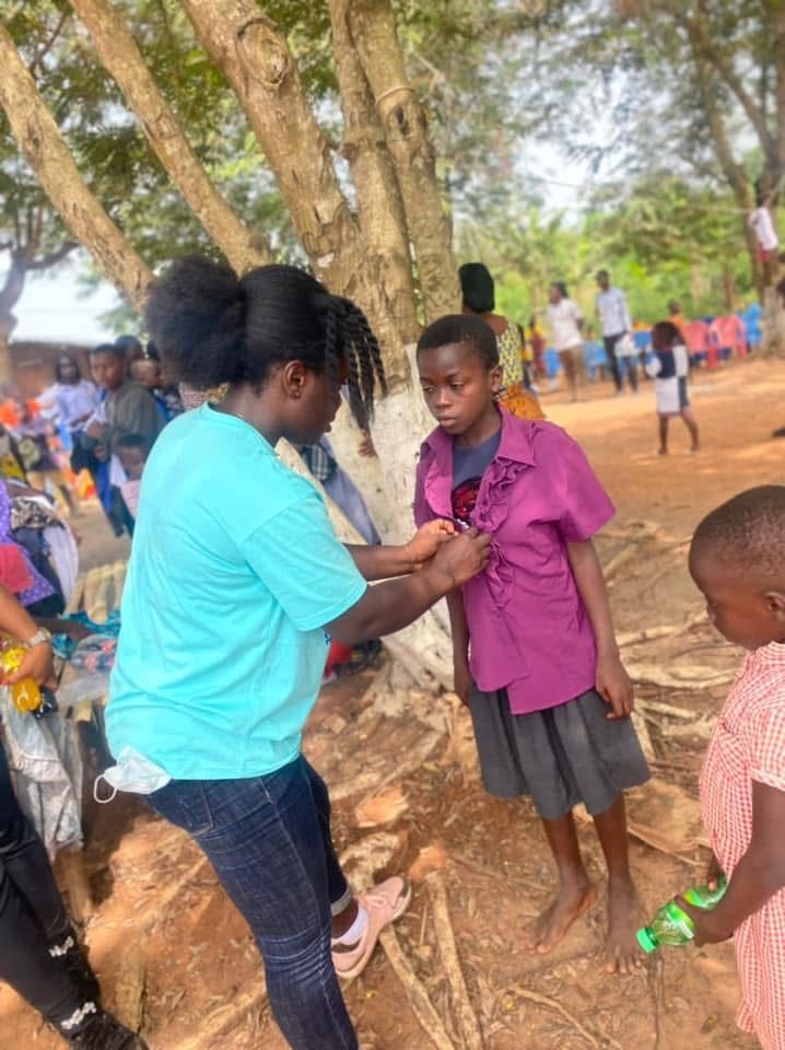A volunteer in a teal foundation T-shirt buttons a new purple blouse for a girl.