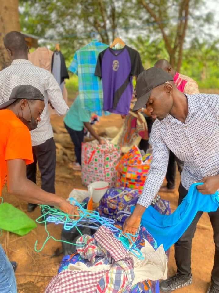 Volunteers sort through bags of donated clothing outdoors, with shirts hung up on hangers behind them.