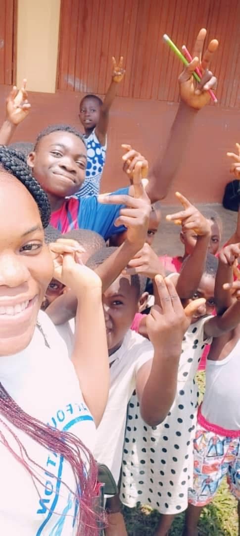 A volunteer takes a selfie with a crowd of cheerful children making peace signs.
