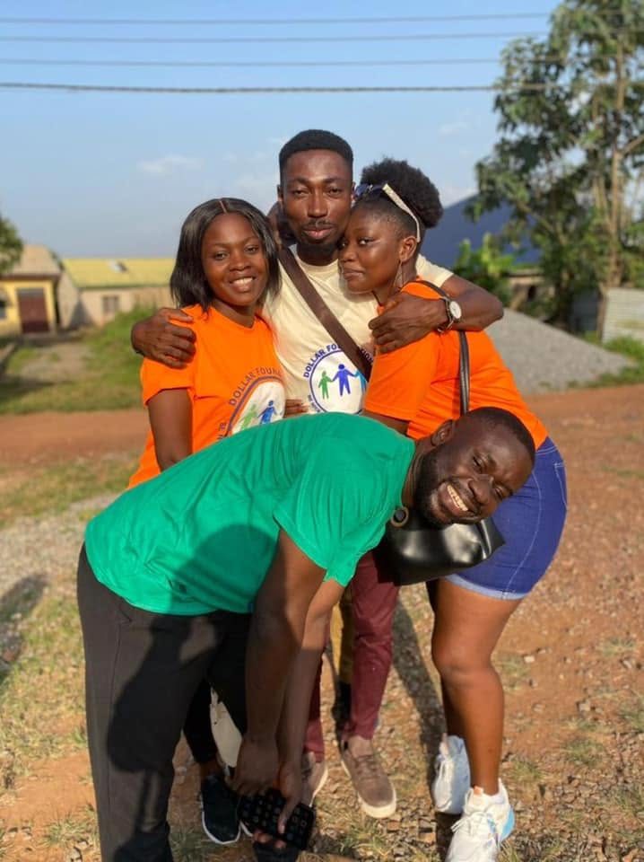 Four volunteers in a laughing group hug outdoors.