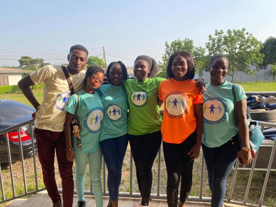 Six volunteers smiling side by side on a veranda in foundation T-shirts.
