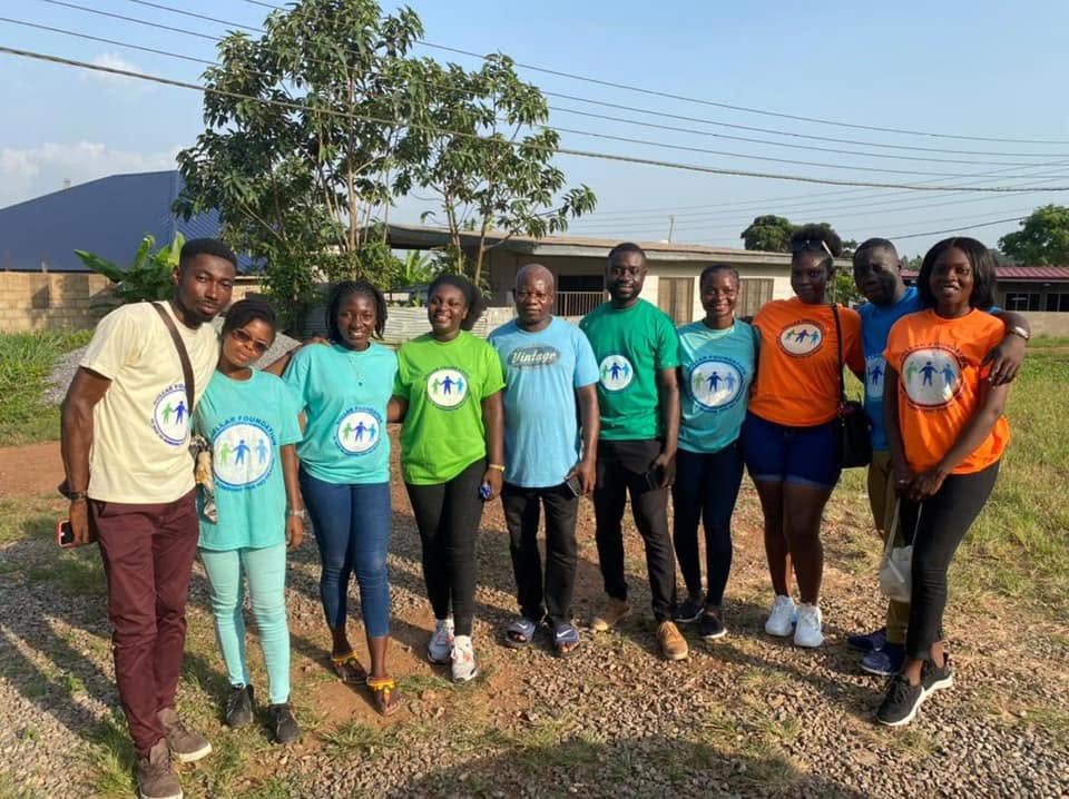 Eleven Dollar Foundation volunteers standing together outdoors in green, blue, orange and cream foundation T-shirts, smiling.
