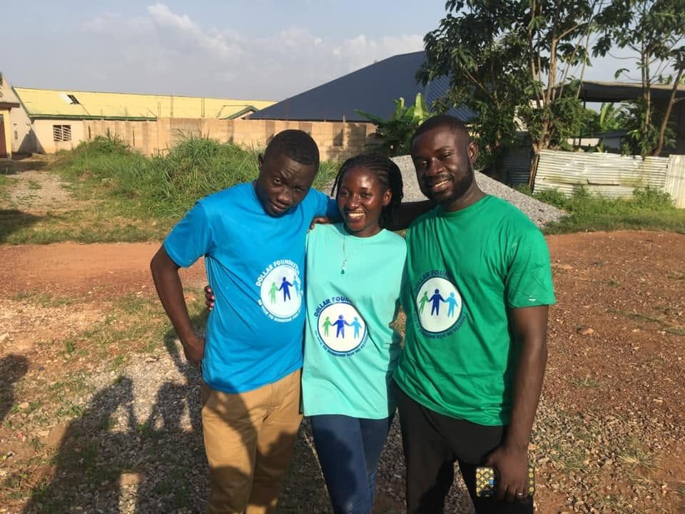 Three volunteers in blue, teal and green foundation T-shirts with their arms around each other.