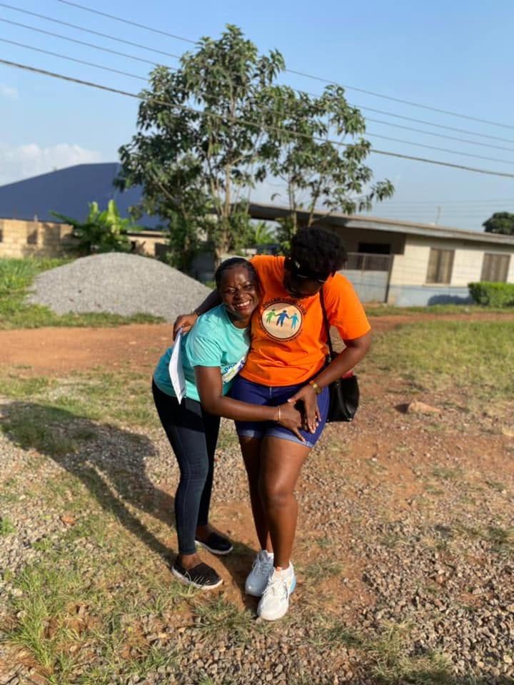 Two volunteers in teal and orange foundation T-shirts hugging and smiling.